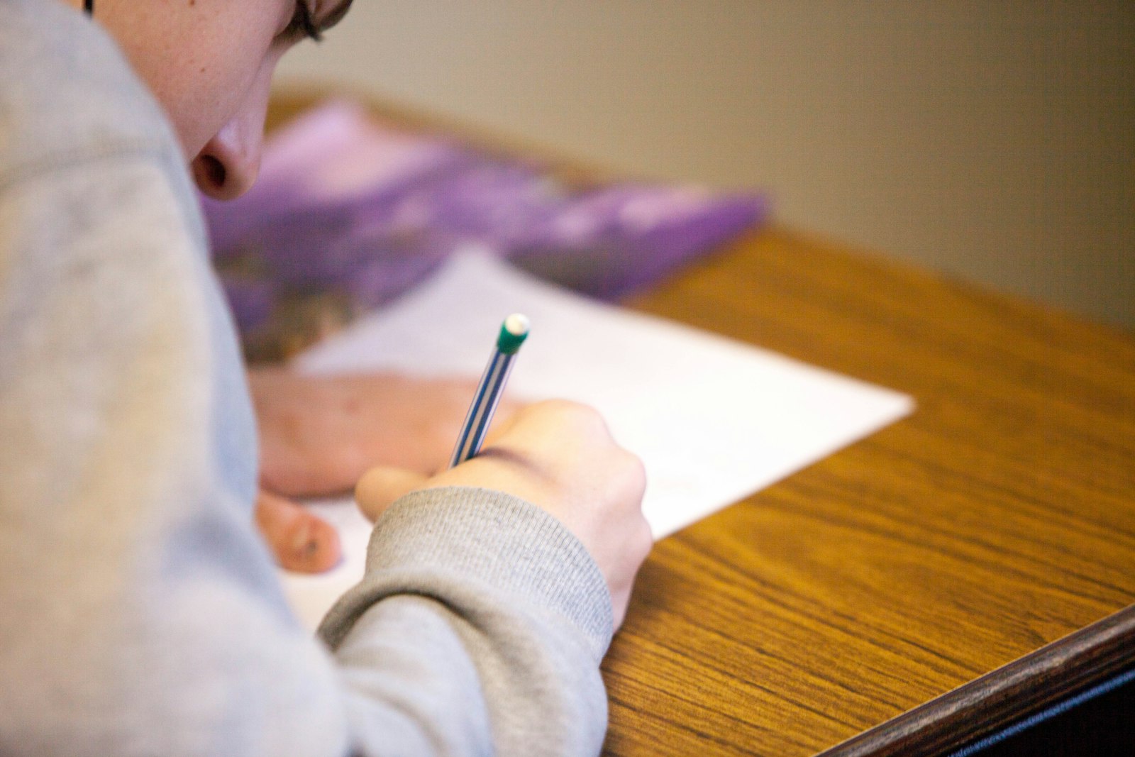 Student writing answers on a test paper at a desk